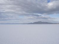 a large expanse full of snow in the desert with mountains in the background under cloudy skies