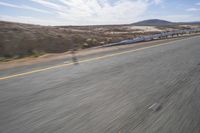 a person riding on the road in the desert near the mountains and train track with the sun shining