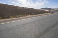 a person riding on the road in the desert near the mountains and train track with the sun shining