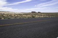 a highway going through an empty desert area with bushes and rocks in the distance and a lone building sits on the horizon