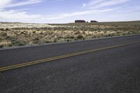 a highway going through an empty desert area with bushes and rocks in the distance and a lone building sits on the horizon