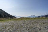 a rocky mountain with green grass, with mountains in the background and a few small hills