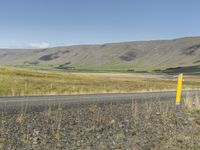 a long road leading through the grass covered hills in the distance is a large river