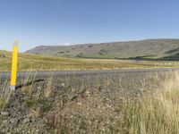 a long road leading through the grass covered hills in the distance is a large river