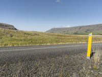 a long road leading through the grass covered hills in the distance is a large river