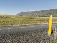 a long road leading through the grass covered hills in the distance is a large river