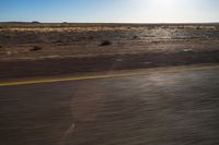 the view from the windshield of an oncoming motorcycle with open desert in background and sunbursted area