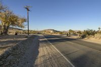 a road with power lines next to trees and bushes in the desert area by a telephone pole