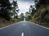 the empty road is lined with trees and rocks and is shown with no people or vehicles