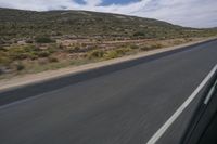 a person riding a motorcycle on a long highway in the desert, with a mountain backdrop