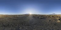 the camera has a bright halo in the blue sky above a dirt road with rocks and a mountain behind it