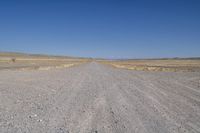 a dirt road in the distance with no cars on it and dry grass near each side