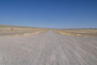 a dirt road in the distance with no cars on it and dry grass near each side