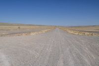 a dirt road in the distance with no cars on it and dry grass near each side