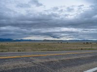 a long street passes a prairie area and mountains in the distance with heavy clouds in the sky