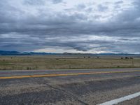 a long street passes a prairie area and mountains in the distance with heavy clouds in the sky