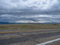 a long street passes a prairie area and mountains in the distance with heavy clouds in the sky