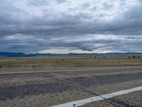 a long street passes a prairie area and mountains in the distance with heavy clouds in the sky