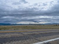 a long street passes a prairie area and mountains in the distance with heavy clouds in the sky