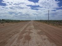 an empty dirt road near a cross on a cloudy day outside a desert plain area