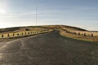 an empty road with a dirt and grassy mountain on both sides and barbed wooden posts