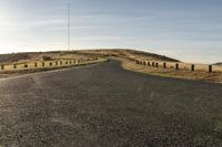 an empty road with a dirt and grassy mountain on both sides and barbed wooden posts