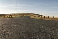 an empty road with a dirt and grassy mountain on both sides and barbed wooden posts