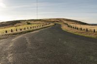 an empty road with a dirt and grassy mountain on both sides and barbed wooden posts