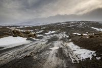 snow covered road on rocky hillside with dark clouds in background with sky covered with snow