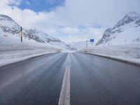 the snow has fallen on both sides of an empty road and mountain peaks in the background