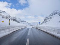 the snow has fallen on both sides of an empty road and mountain peaks in the background