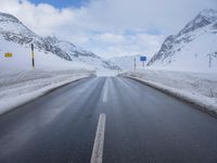 the snow has fallen on both sides of an empty road and mountain peaks in the background