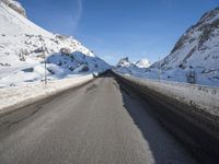 an empty highway is lined with mountains with snow and the road is long and flat