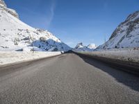 an empty highway is lined with mountains with snow and the road is long and flat