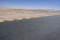 an empty road near a desert landscape with a person riding a bike on it on a clear day