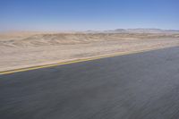 an empty road near a desert landscape with a person riding a bike on it on a clear day