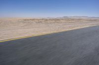 an empty road near a desert landscape with a person riding a bike on it on a clear day