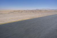 an empty road near a desert landscape with a person riding a bike on it on a clear day