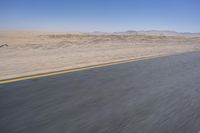 an empty road near a desert landscape with a person riding a bike on it on a clear day