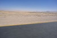 an empty road near a desert landscape with a person riding a bike on it on a clear day