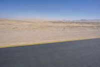 an empty road near a desert landscape with a person riding a bike on it on a clear day
