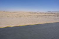 an empty road near a desert landscape with a person riding a bike on it on a clear day