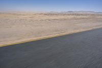 an empty road near a desert landscape with a person riding a bike on it on a clear day