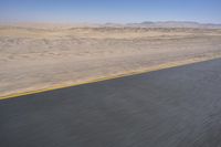 an empty road near a desert landscape with a person riding a bike on it on a clear day