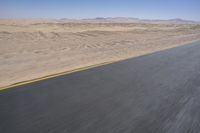 an empty road near a desert landscape with a person riding a bike on it on a clear day