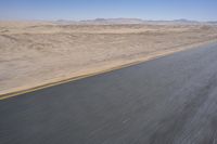an empty road near a desert landscape with a person riding a bike on it on a clear day