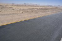 an empty road near a desert landscape with a person riding a bike on it on a clear day