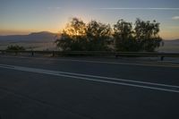 the road is empty and the traffic lights on as the sun sets over mountains in the distance