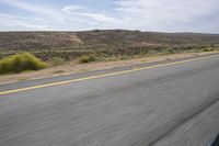 the motorcycle is riding on the highway through the desert plains, with mountains in the back