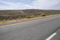 the motorcycle is riding on the highway through the desert plains, with mountains in the back